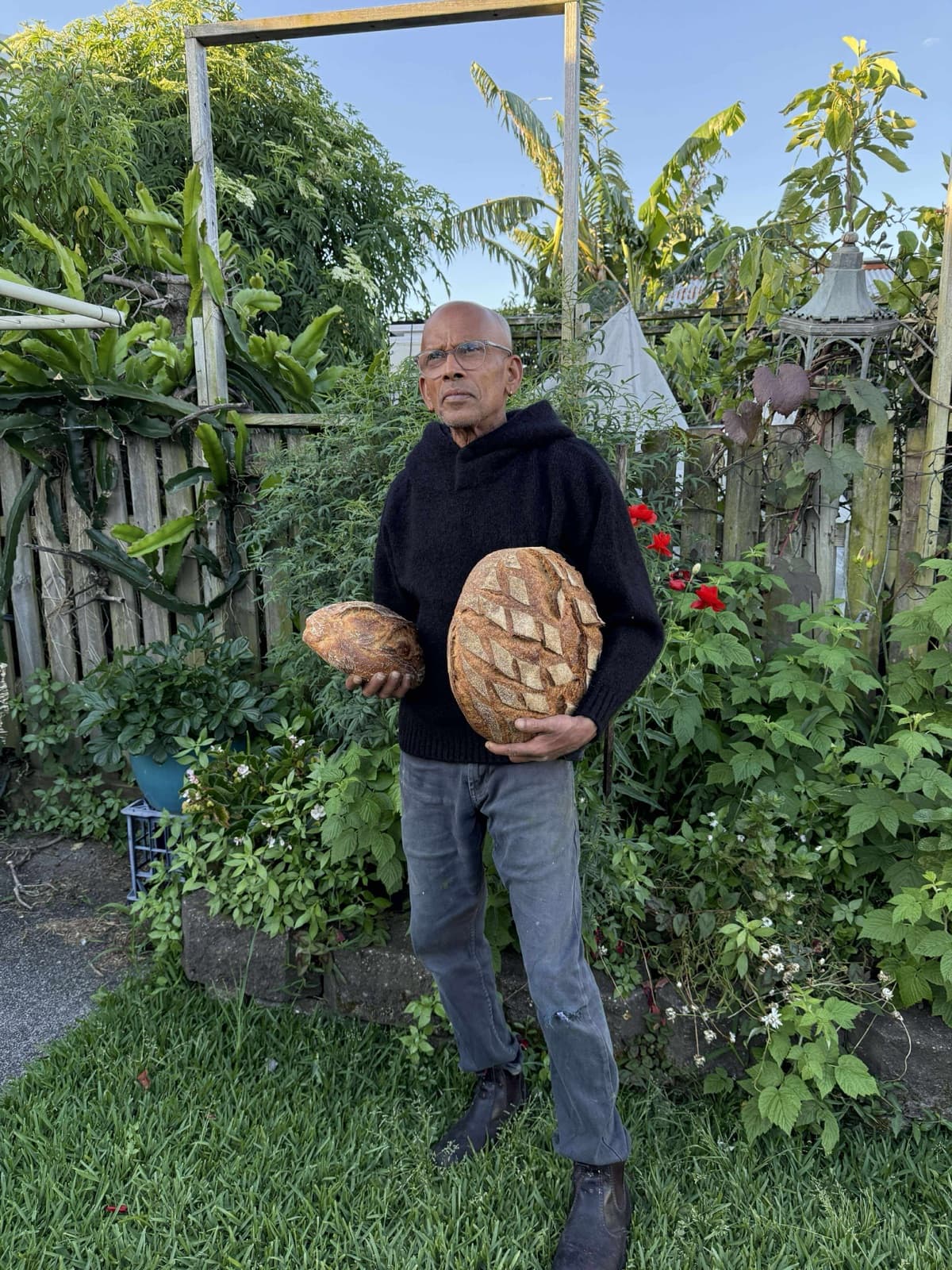Joseph in his garden holding two sourdough loaves